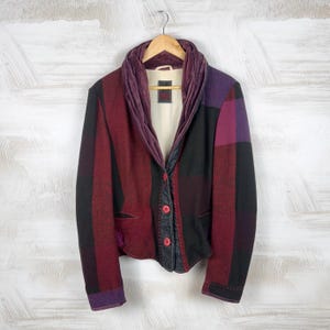 May include: A patchwork jacket in shades of burgundy, black, and purple, hanging on a wooden hanger. The jacket features a velvet collar and red buttons. The design includes a mix of striped and solid fabric panels.