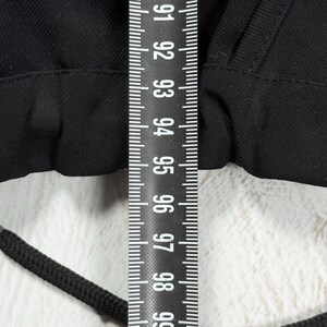 May include: A black garment featuring a drawstring waistband with a black cord, positioned beneath a vertical measuring tape that displays numerical markings from 91 to 99 centimeters, indicating the width of the fabric section shown.