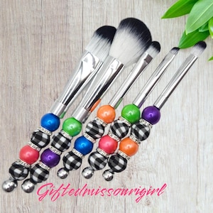 May include: Set of five makeup brushes with black and white checkered handles and colorful beads. The brushes have silver metal handles and different sized brush heads.