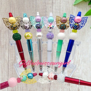 May include: Seven colorful pens with butterfly-shaped tops and various bead embellishments. The pens are displayed on a clear plastic stand. The text "Giftfrommissourigirl" is visible at the bottom of the image.