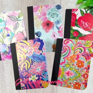 May include: Five notebooks with floral designs. The covers feature various colorful patterns, including pink, blue, and red flowers, and paisley. Each notebook has a black spine and a white or light-colored background.