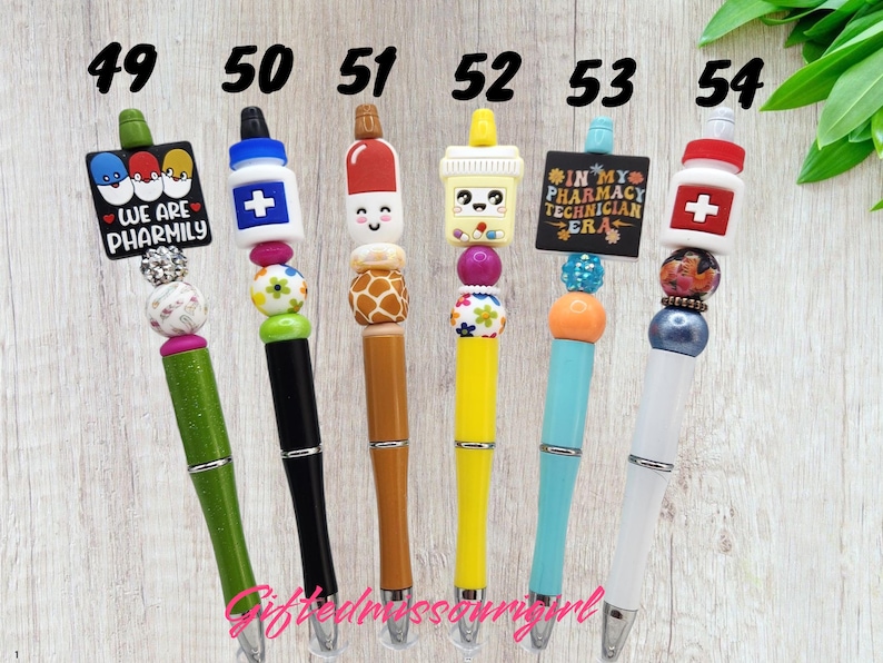 K&ouml;nnte beinhalten: Eine Sammlung von sechs dekorativen Stiften mit einzigartigen Designs. Jeder Stift verf&uuml;gt &uuml;ber einen farbenfrohen Perlenakzent und einen thematischen Aufsatz, darunter eine Apothekenflasche, eine Kaffeetasse und der Text "WE ARE PHARMILY" und "IN MY PHARMACY TECHNICIAN ERA".