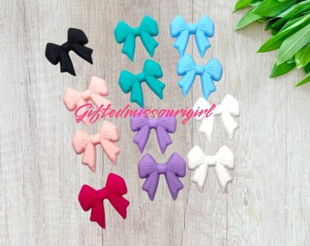 May include: A collection of colorful bow-shaped embellishments in various shades, including black, teal, light blue, pink, purple, and white. The text "Giftedmissourigirl" is visible. These bows are likely for crafts or accessories.