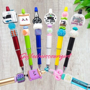 May include: A collection of decorative pens with various sewing-themed toppers. The pens feature designs such as sewing machines, spools of thread, and scissors. The pens come in a variety of colors, including red, green, blue, and yellow.