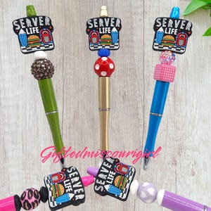 May include: Three decorative pens with the text "SERVER LIFE" on the top. The pens have different colored barrels: green, gold, and blue. Each pen has a unique decorative top, including a rhinestone ball, a red polka-dot ball, and a pink square design.