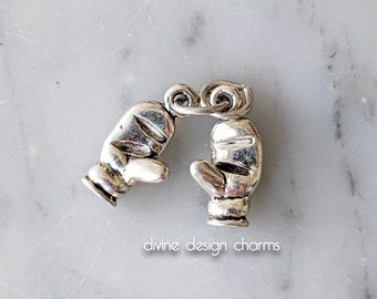May include: Two silver charm pendants in the shape of mittens. The mittens are connected by a silver loop.