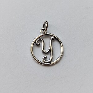 May include: Silver charm with a circle design featuring a cursive letter Y.