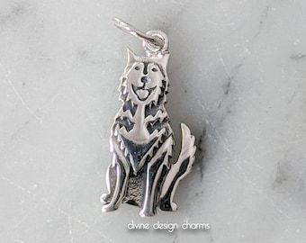 May include: A silver-colored charm in the shape of a sitting dog, possibly a husky, with a happy expression. The charm has detailed fur and a loop for attaching to a bracelet or necklace. The text "divine design charms" is at the bottom.