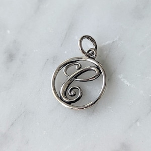 May include: Silver charm with a cursive letter C in a circle.