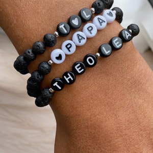 Peut inclure: Trois bracelets en pierre de lave noire avec des perles de lettres blanches qui épellent les noms "Theo", "Papa" et "Lea". Chaque bracelet a un petit charme en forme de cœur blanc.