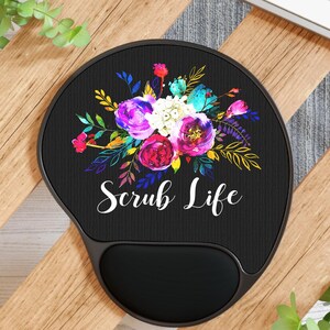 May include: Black ergonomic mouse mat featuring a floral design in purple, pink, blue, and yellow. The words "Scrub Life" are written in white script below the flowers. The mat has a built-in wrist rest.
