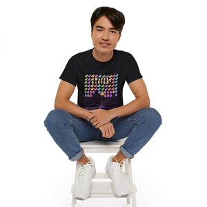 May include: Black t-shirt featuring a colorful graphic design with the text "HAPPY EASTER!" and rows of bunnies. The design has a retro video game aesthetic. The person is wearing blue jeans and white sneakers.