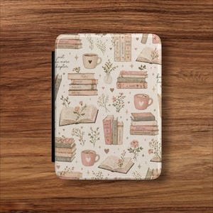 May include: A cream-colored e-reader cover with a repeating pattern of books, coffee cups, and floral accents. The cover features the text "Just one more chapter" and is designed to protect the device.