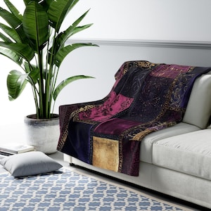 May include: A patchwork throw blanket draped over a white sofa. The blanket features squares of deep purple, gold, and fuchsia, with ornate patterns and gold trim. A large potted plant is in the background.