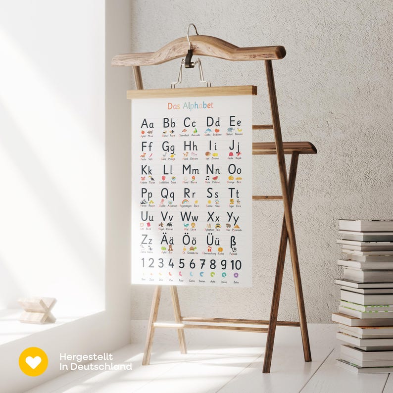 May include: A wooden easel displaying a white educational poster with the German alphabet and numbers 1-10. The poster has colorful illustrations and is held by a wooden hanger. The text "Das Alphabet" is at the top.