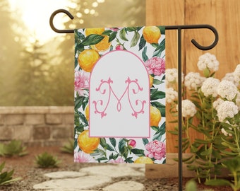 Peut inclure: Un drapeau de jardin avec un fond blanc et un monogramme rose "M" dans une police décorative. Le drapeau présente un motif floral avec des fleurs roses et des feuilles vertes, et des citrons jaunes.