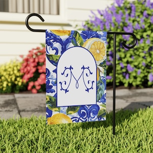 May include: A garden flag with a blue and white tiled pattern featuring lemons and a white arch with the letter "M" in blue.