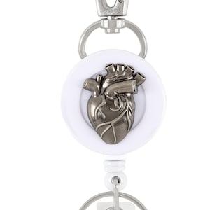 May include: White retractable badge reel with a silver heart-shaped charm. The charm is a detailed anatomical heart.