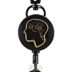 May include: Black retractable badge reel with a black metal clip and a black round badge holder featuring a gold silhouette of a head with gears inside.