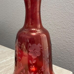 May include: A deep red glass vase with a wide base and a narrow neck. The vase is etched with a floral design.