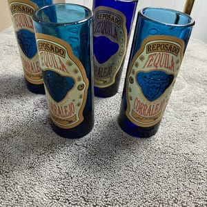 May include: Four blue shot glasses with a gold label that reads "Reposado Tequila Corralejo".