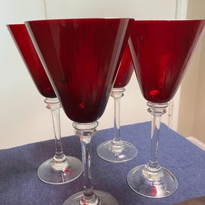 May include: Four red-tinted martini glasses with clear stems and bases. The glasses have a classic conical bowl shape. The stems feature a decorative bulbous detail. The glasses are arranged on a blue surface.