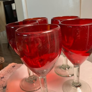 Pode incluir: Um conjunto de cinco taças de vinho tinto. As taças têm um design clássico com uma taça arredondada e uma haste e base transparentes. A cor vermelha do vidro é vibrante e translúcida, sugerindo que são feitas de vidro colorido.