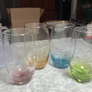 May include: Four clear glass tumblers with a textured surface. Each tumbler has a different colored bottom: pink, orange, blue, and green.