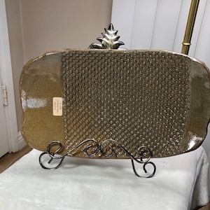 May include: A brown ceramic serving tray with a textured surface. The tray is on a black metal stand with a decorative scroll design.