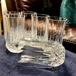 May include: A set of six clear glass tumblers featuring a vertical ribbed pattern on the upper portion and a diamond-cut geometric texture around the base. The glasses are arranged with five standing upright and one lying horizontally in the front.