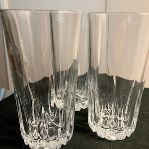 May include: Three clear, patterned drinking glasses. The glasses have a textured, cut-glass design with vertical and geometric patterns. The glasses are made of transparent glass and are displayed on a dark surface.