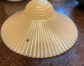 May include: A vintage, off-white glass lampshade with a ribbed, scalloped design. The shade has a conical top and a flared, circular bottom. A small hole is visible near the edge. The shade is likely from a mid-century modern lamp.