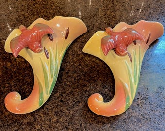 May include: Two vintage wall pocket vases. Each vase is shaped like a horn with a curved base and a flared top. The vases are painted in shades of yellow, orange, and red, with a bird and cattails design. The vases are approximately 10 inches tall.
