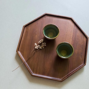 Peut inclure: Un plateau de service octogonal en bois, de couleur marron foncé. Deux petites tasses en céramique verte avec des bords dorés sont posées sur le plateau, ainsi qu'une brindille de fleurs séchées. Le plateau est vide et prêt à l'emploi.