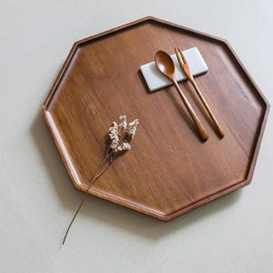Peut inclure: Un plateau octogonal en bois avec une finition marron foncé. Une cuillère et une fourchette en bois reposent sur une petite tuile rectangulaire blanche. Une brindille de fleurs séchées est placée sur le plateau.