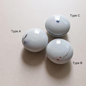 May include: Three white ceramic decorative containers. Type A has a dark brown and grey design. Type B has a red and green floral design. Type C has a blue floral design and a black band.