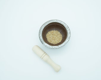 May include: A white ceramic mortar and pestle with a brown interior. The mortar is filled with sesame seeds.