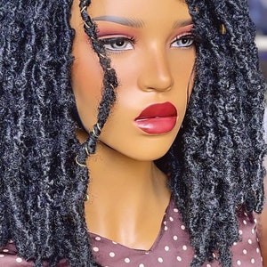 Puede incluir: Una peluca negra con rastas sueltas y rizadas, con estilo bob. La peluca tiene anillos dorados tejidos en las rastas.