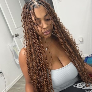 May include: A woman with long, brown, curly hair styled in twists. She is wearing a light gray tank top and a silver necklace with a cross pendant.