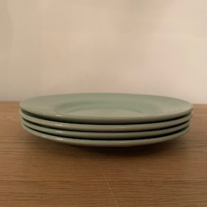 Pode incluir: Uma pilha de quatro pratos de cerâmica verde claro. Os pratos têm uma textura ligeiramente ondulada.
