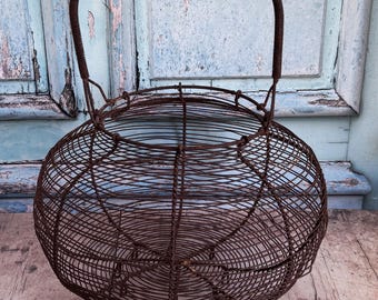 Puede incluir: Una cesta redonda de alambre, con asa, de metal marrón oscuro. La cesta tiene forma esférica y un diseño tejido. Dos llaves antiguas están sobre una superficie de madera. El fondo muestra una puerta azul claro desgastada. Diámetro aproximado: 30 cm.