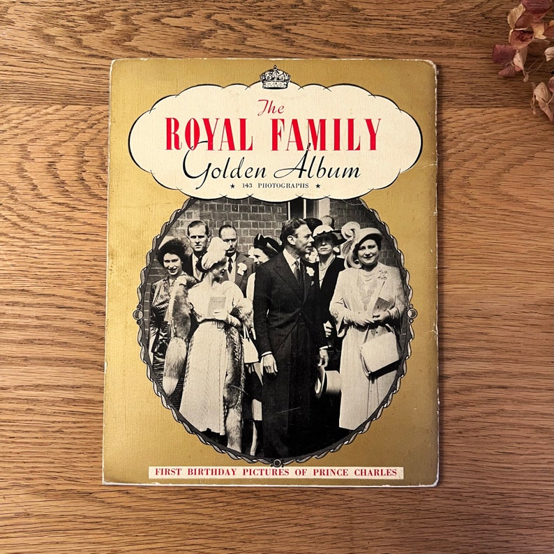 May include: A vintage book titled "The Royal Family Golden Album" with a black and white photo of the royal family on the cover. The book features a gold background and the text "143 Photographs" and "First Birthday Pictures of Prince Charles".