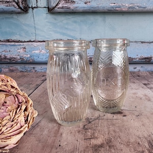 May include: Two clear glass OXO jars with textured vertical lines and embossed text. One jar has a clear OXO label. The jars are on a wooden surface with a dried flower arrangement in the foreground.