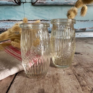 May include: Two clear glass jars with ribbed textures. The jars have labels with the word "Pomona" printed on them. The jars are sitting on a wooden surface.