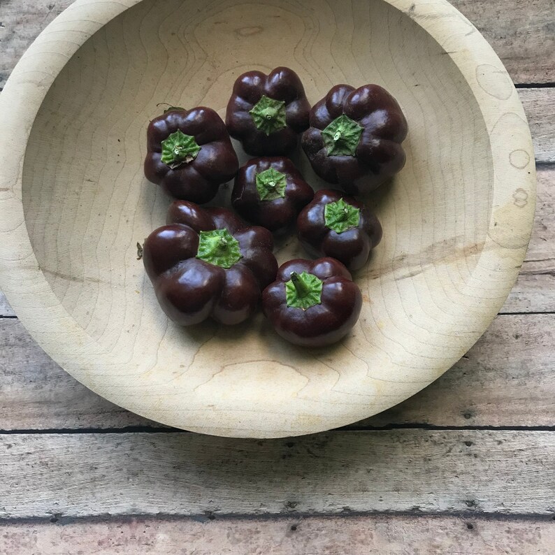 May include: A wooden bowl filled with dark purple bell peppers. The peppers have green stems and are arranged in a circular pattern.