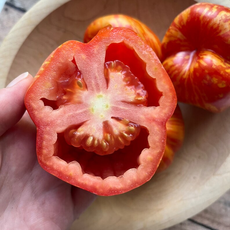 May include: A red tomato cut in half, revealing the inside with seeds. The tomato has a yellow and red striped pattern on the outside.
