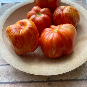 May include: A wooden bowl filled with five red and yellow striped heirloom tomatoes.