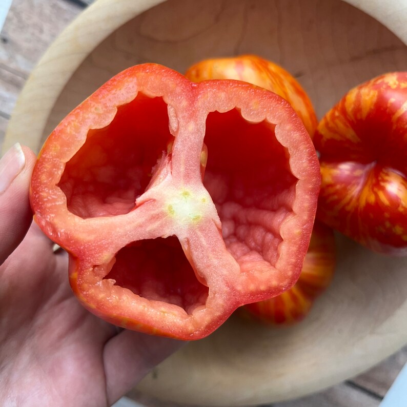 May include: A red tomato cut in half, revealing the inside with three chambers. The tomato has a striped pattern of yellow and red.