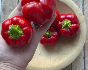 May include: Four red bell peppers in a wooden bowl. The peppers are all about the same size and are a bright red color. The bowl is made of light wood and has a natural finish.