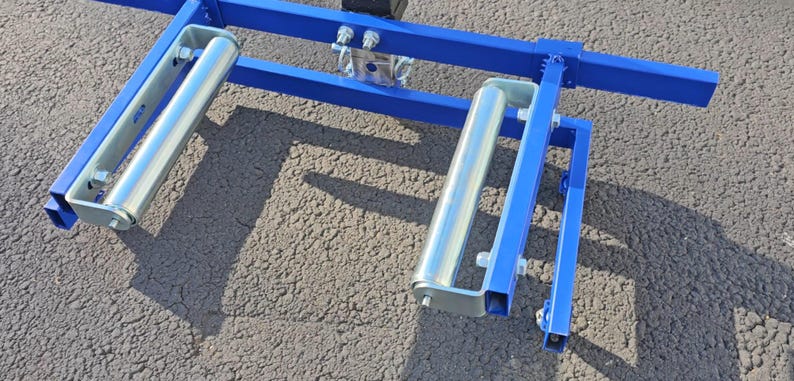 Puede incluir: Un marco de metal azul con dos rodillos plateados. El marco est&aacute; dise&ntilde;ado para soportar y mover objetos pesados.